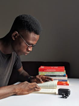 Young man studying intently with books in library setting.